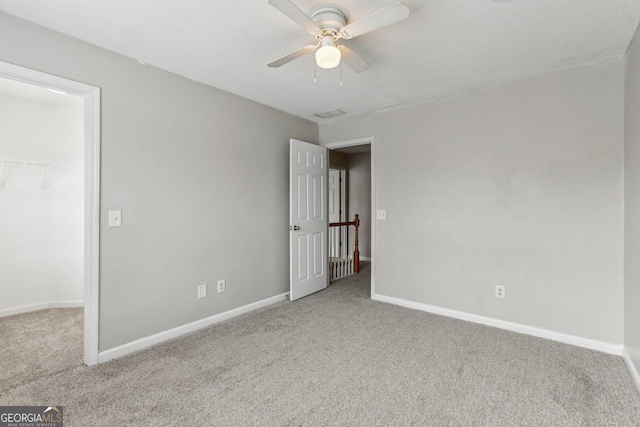 unfurnished bedroom with ceiling fan, a walk in closet, carpet flooring, and a textured ceiling