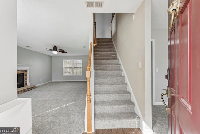 stairway with ceiling fan, a fireplace, and carpet