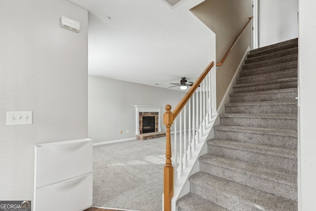 stairs with ceiling fan, carpet flooring, and a textured ceiling