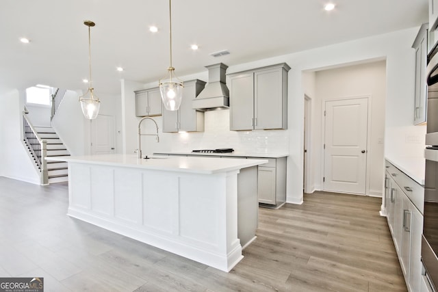 kitchen featuring premium range hood, hanging light fixtures, a kitchen island with sink, sink, and gray cabinets