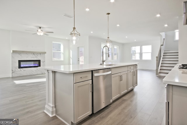 kitchen featuring sink, hanging light fixtures, stainless steel dishwasher, gray cabinetry, and a center island with sink