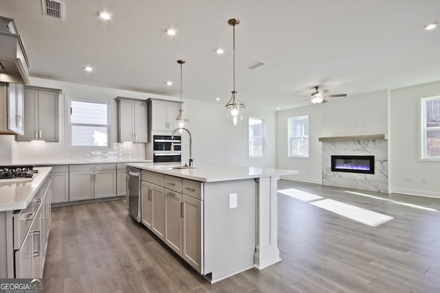 kitchen with a center island with sink, decorative backsplash, hanging light fixtures, and stainless steel appliances