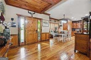 foyer featuring beam ceiling, wood ceiling, wooden walls, light hardwood / wood-style flooring, and crown molding