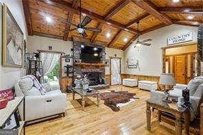 living room featuring a fireplace, light wood-type flooring, vaulted ceiling with beams, and ceiling fan