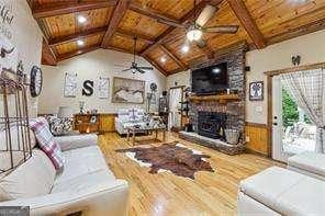 living room with wood ceiling, ceiling fan, a stone fireplace, and vaulted ceiling with beams