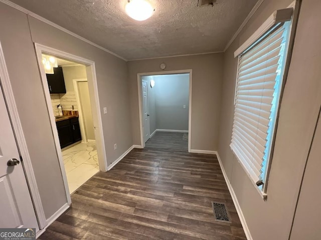 hall featuring baseboards, visible vents, dark wood-style floors, ornamental molding, and a textured ceiling