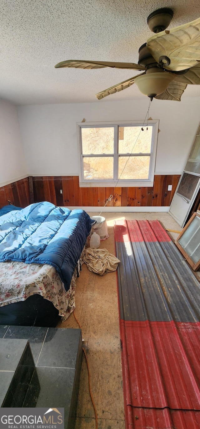 bedroom featuring wood walls, a textured ceiling, and ceiling fan