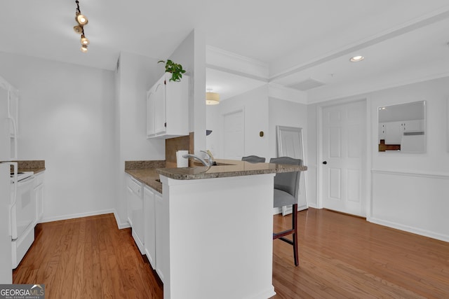 kitchen with light hardwood / wood-style flooring, a breakfast bar area, white cabinets, and kitchen peninsula