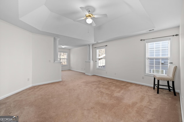 carpeted empty room with ceiling fan, a tray ceiling, and ornate columns