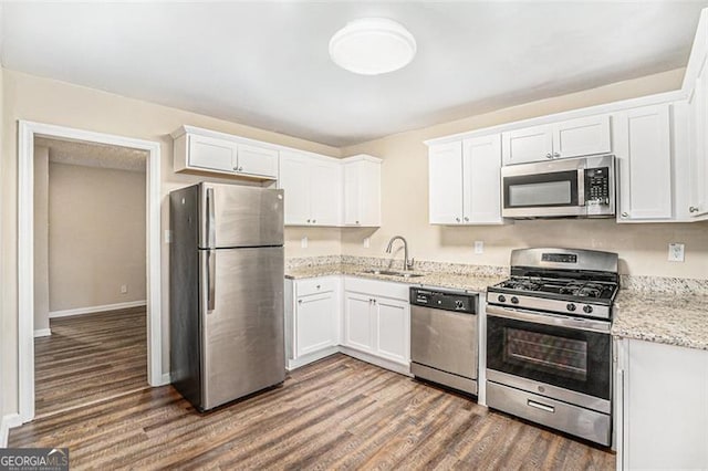 kitchen with appliances with stainless steel finishes, white cabinetry, sink, dark hardwood / wood-style flooring, and light stone counters