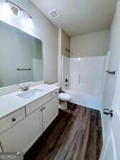 full bathroom featuring hardwood / wood-style flooring, vanity, toilet, and shower / washtub combination