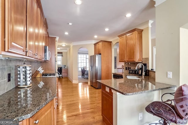 kitchen with appliances with stainless steel finishes, dark stone countertops, sink, ornamental molding, and kitchen peninsula