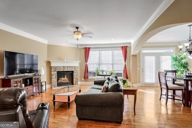 living room with ceiling fan with notable chandelier, a stone fireplace, hardwood / wood-style floors, and crown molding