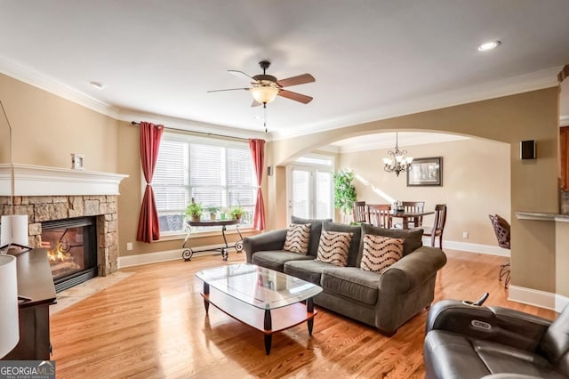 living room with ceiling fan with notable chandelier, ornamental molding, light hardwood / wood-style floors, and a fireplace