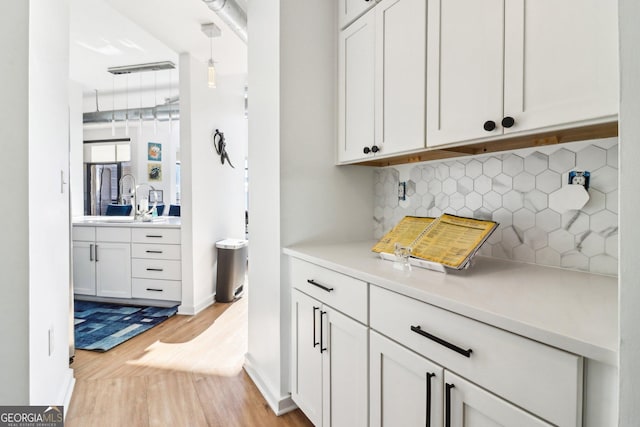 bar featuring tasteful backsplash, white cabinets, light wood-type flooring, sink, and pendant lighting