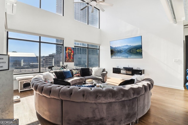 living room with ceiling fan, light hardwood / wood-style flooring, and a towering ceiling