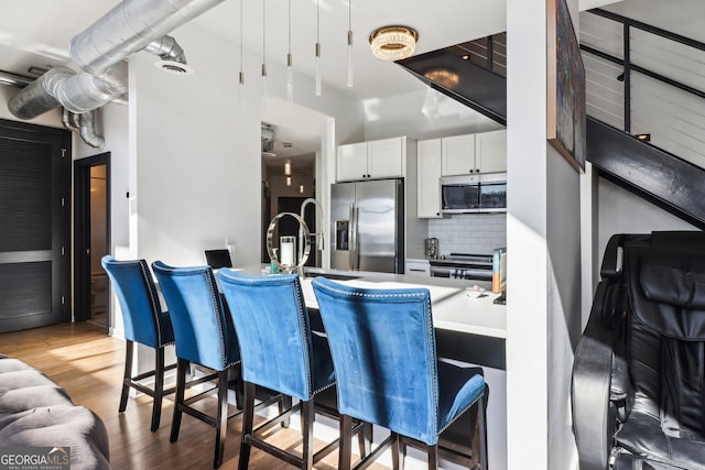 kitchen with backsplash, white cabinetry, light wood-type flooring, and stainless steel appliances