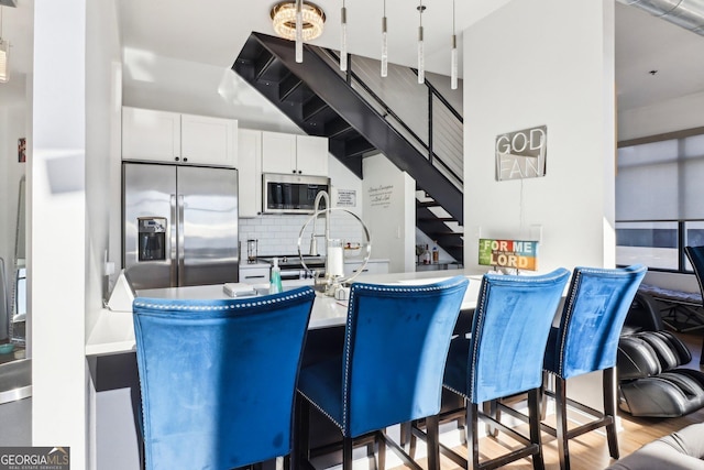 kitchen with decorative light fixtures, backsplash, white cabinetry, light hardwood / wood-style floors, and stainless steel appliances