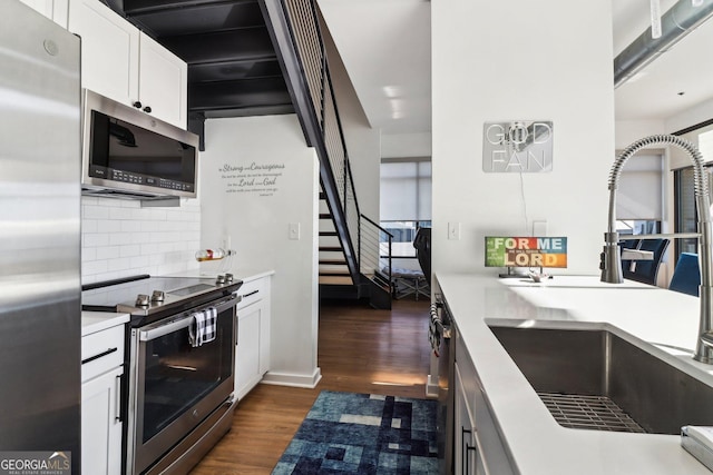 kitchen with appliances with stainless steel finishes, decorative backsplash, white cabinets, sink, and dark hardwood / wood-style flooring