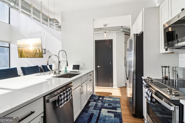 kitchen with white cabinetry, sink, light hardwood / wood-style flooring, pendant lighting, and stainless steel appliances