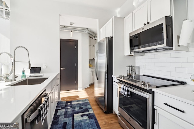 kitchen with white cabinets, appliances with stainless steel finishes, sink, backsplash, and light hardwood / wood-style flooring