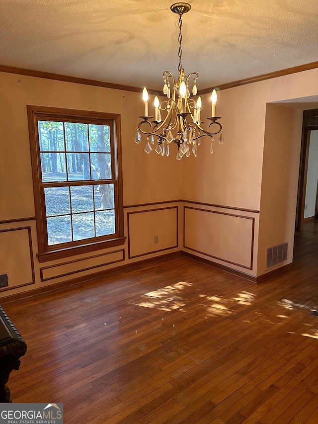 unfurnished dining area featuring a chandelier, dark wood-type flooring, a textured ceiling, and ornamental molding