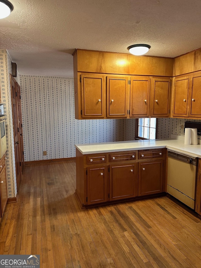 kitchen featuring light hardwood / wood-style floors, a textured ceiling, dishwasher, and kitchen peninsula