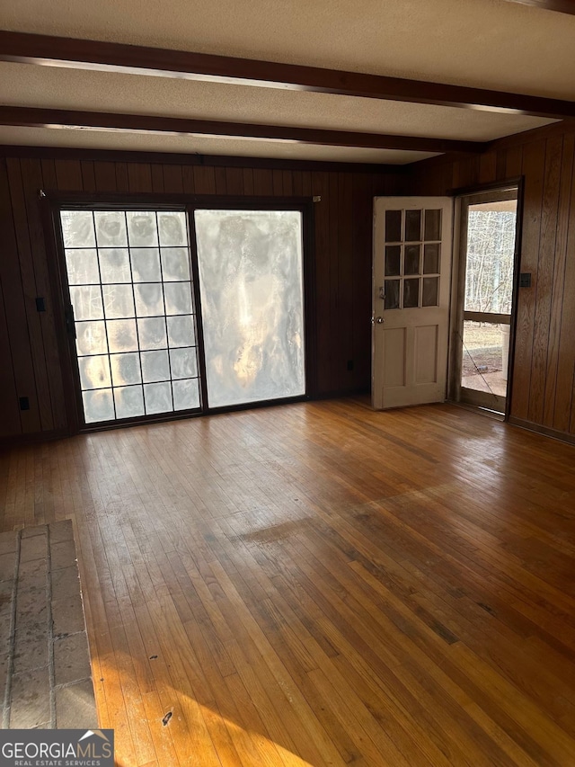 unfurnished living room with wood walls, beam ceiling, and hardwood / wood-style floors