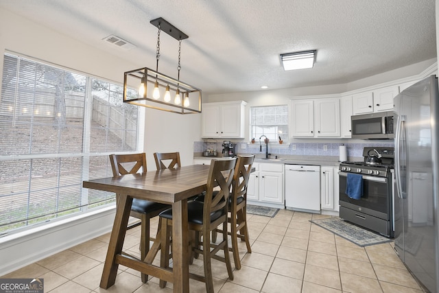 kitchen featuring sink, light tile patterned floors, pendant lighting, stainless steel appliances, and white cabinets