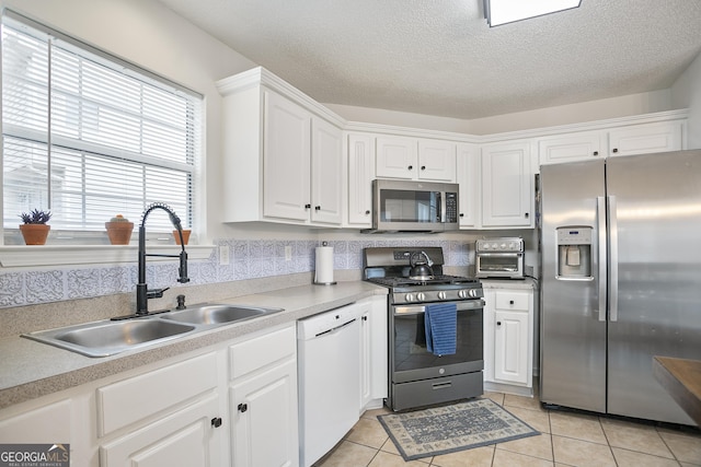 kitchen featuring sink, light tile patterned floors, appliances with stainless steel finishes, white cabinetry, and a textured ceiling