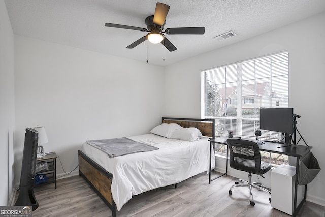 bedroom with ceiling fan, a textured ceiling, and light wood-type flooring