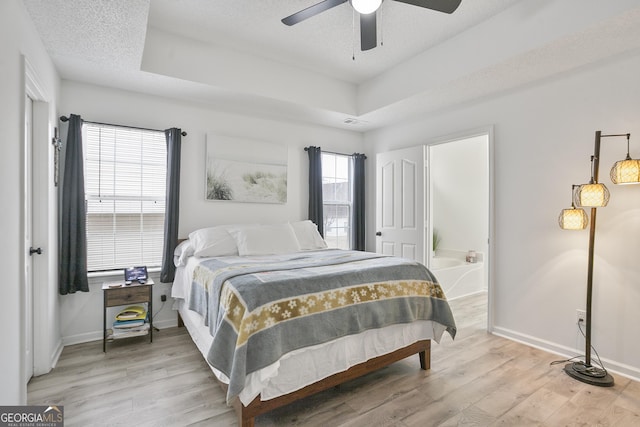 bedroom featuring a tray ceiling, ensuite bath, a textured ceiling, and hardwood / wood-style flooring