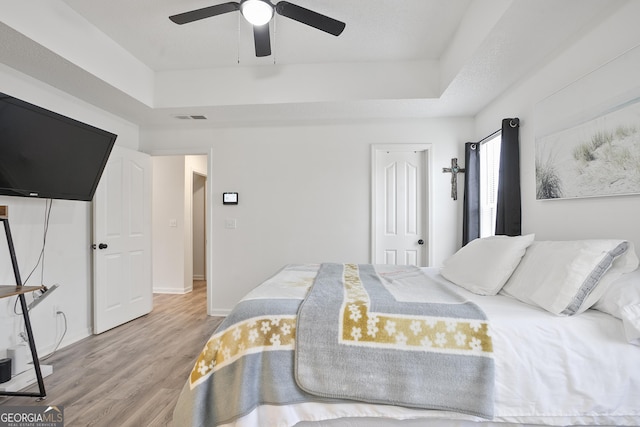 bedroom with a raised ceiling, hardwood / wood-style floors, and ceiling fan