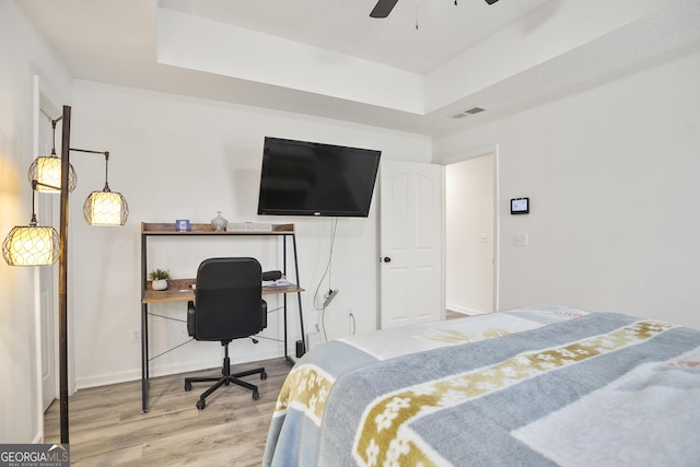 bedroom with wood-type flooring, a raised ceiling, and ceiling fan