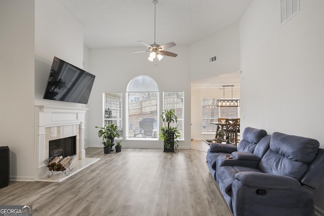 living room featuring high vaulted ceiling, ceiling fan, a high end fireplace, a textured ceiling, and light hardwood / wood-style flooring