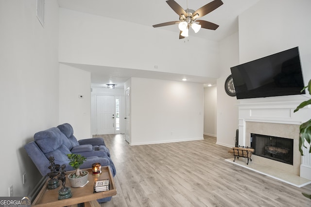 living room with a high ceiling, ceiling fan, a fireplace, and light hardwood / wood-style floors