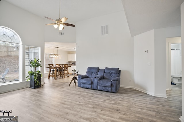 living room with a towering ceiling, ceiling fan, and light wood-type flooring