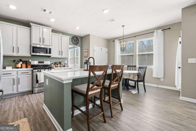 kitchen featuring pendant lighting, appliances with stainless steel finishes, white cabinets, hardwood / wood-style floors, and an island with sink