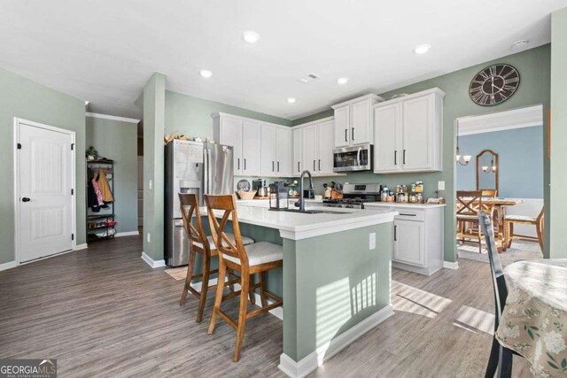 kitchen featuring hanging light fixtures, white cabinets, a kitchen island with sink, a breakfast bar area, and stainless steel appliances