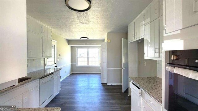 kitchen with dishwasher, white cabinetry, light stone counters, dark hardwood / wood-style floors, and stainless steel oven