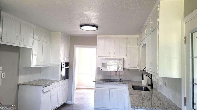 kitchen featuring stainless steel oven, light stone countertops, black electric stovetop, decorative backsplash, and white cabinets