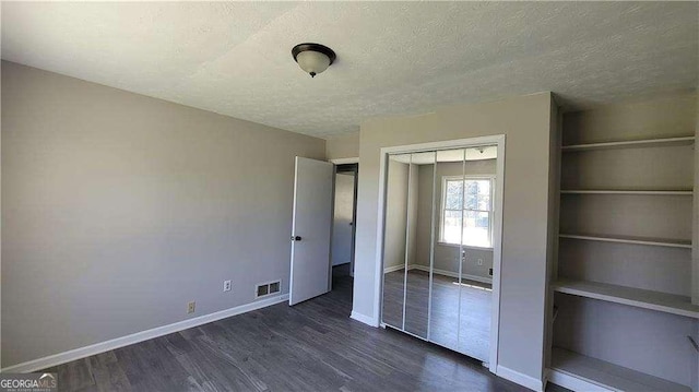 unfurnished bedroom featuring a textured ceiling, a closet, and dark hardwood / wood-style flooring