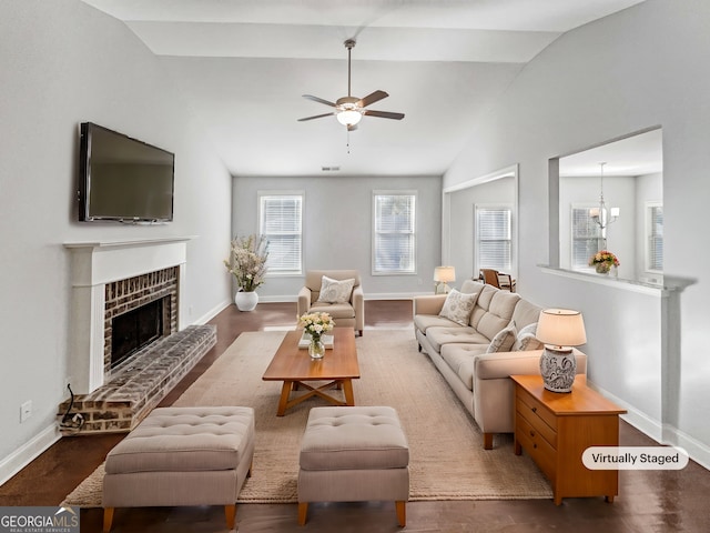 living room featuring a brick fireplace, dark wood-type flooring, lofted ceiling, and ceiling fan with notable chandelier