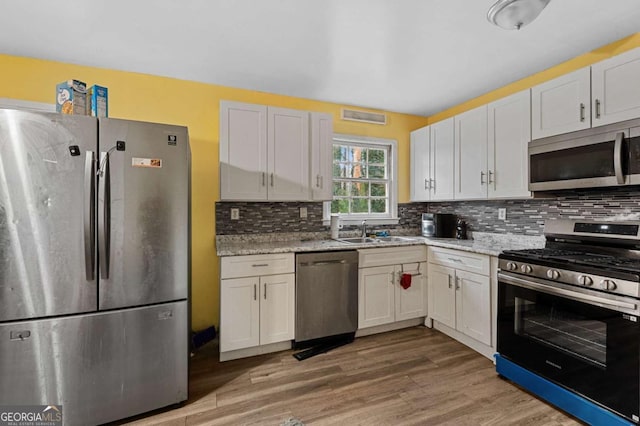 kitchen with light stone countertops, backsplash, white cabinetry, and appliances with stainless steel finishes