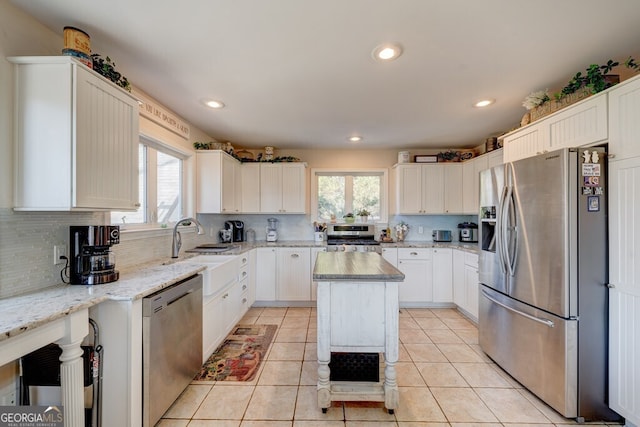 kitchen featuring white cabinetry, stainless steel appliances, a kitchen island, and light stone counters