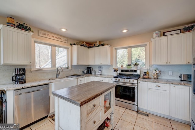 kitchen with appliances with stainless steel finishes, sink, tasteful backsplash, light tile patterned floors, and a center island