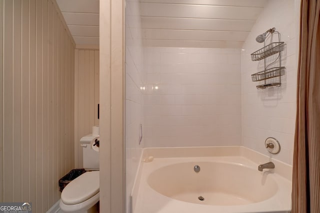 bathroom featuring vaulted ceiling, wood walls, shower / washtub combination, and toilet