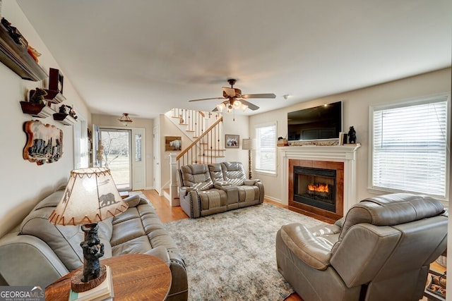 living room featuring light wood-type flooring, ceiling fan, and a tiled fireplace