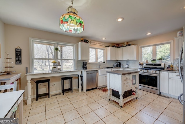 kitchen with appliances with stainless steel finishes, a center island, decorative light fixtures, white cabinetry, and decorative backsplash