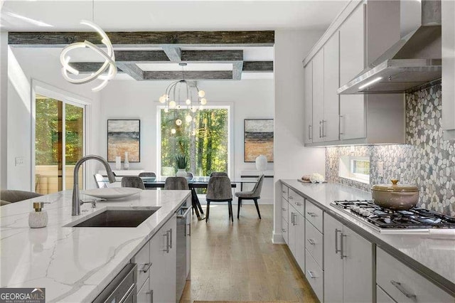 kitchen featuring appliances with stainless steel finishes, white cabinetry, wall chimney range hood, sink, and beam ceiling